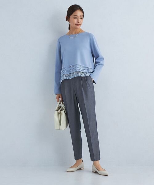 サックスブルーのトップスとグレーのパンツを着た女性