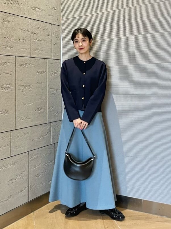 カーディガンとサックスブルーのプリーツスカートを着た女性