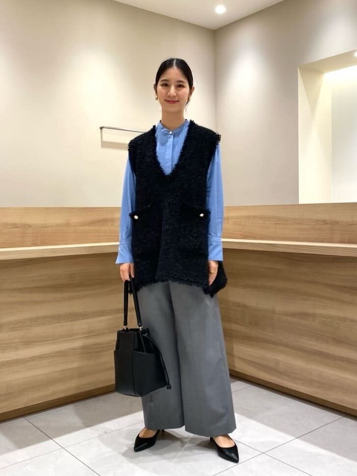 カーディガンとサックスブルーのプリーツスカートを着た女性