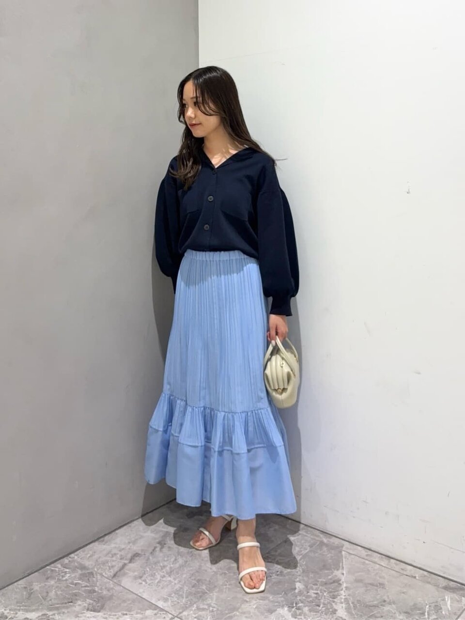 カーディガンとサックスブルーのプリーツスカートを着た女性