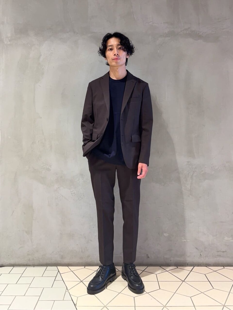 ダークブラウンのジャケットとネイビーのTシャツを着た男性