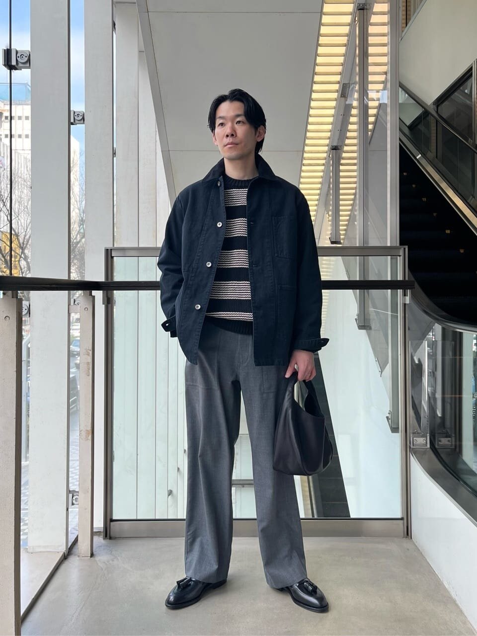 黒のカバーオールとグレーのパンツを着た男性