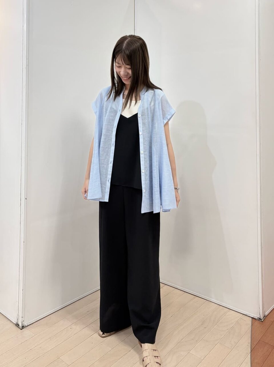 黒のオールインワンに水色のトップスをあわせた女性