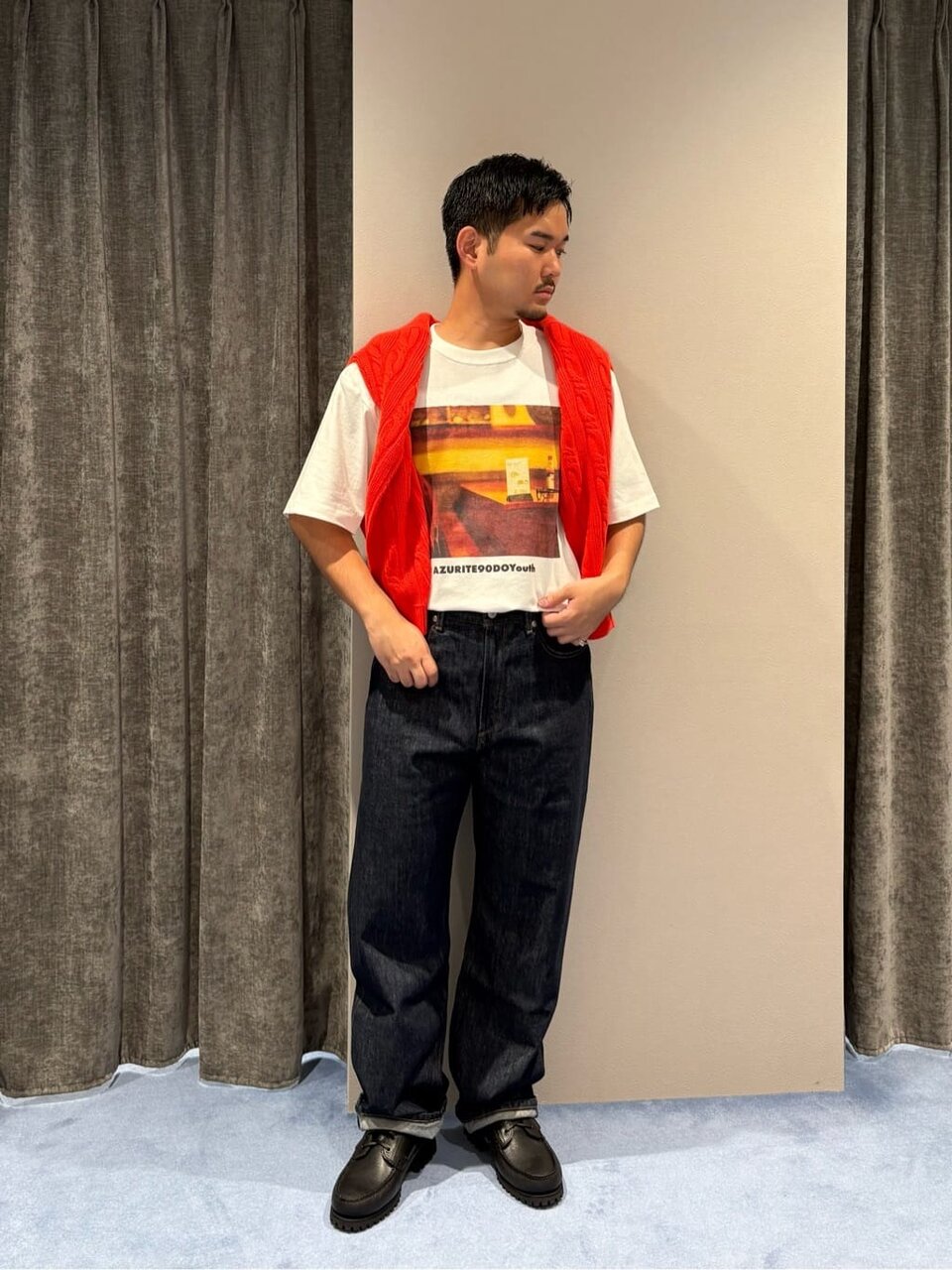 赤のニットを肩掛けした秋服コーデの男性