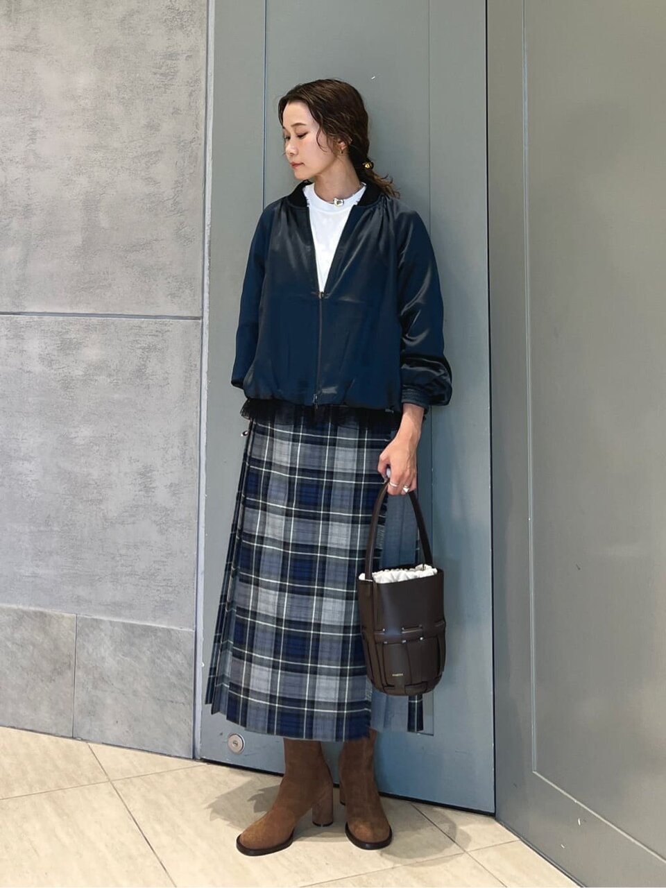 サテンブルゾンとチェック柄プリーツスカートを着た女性